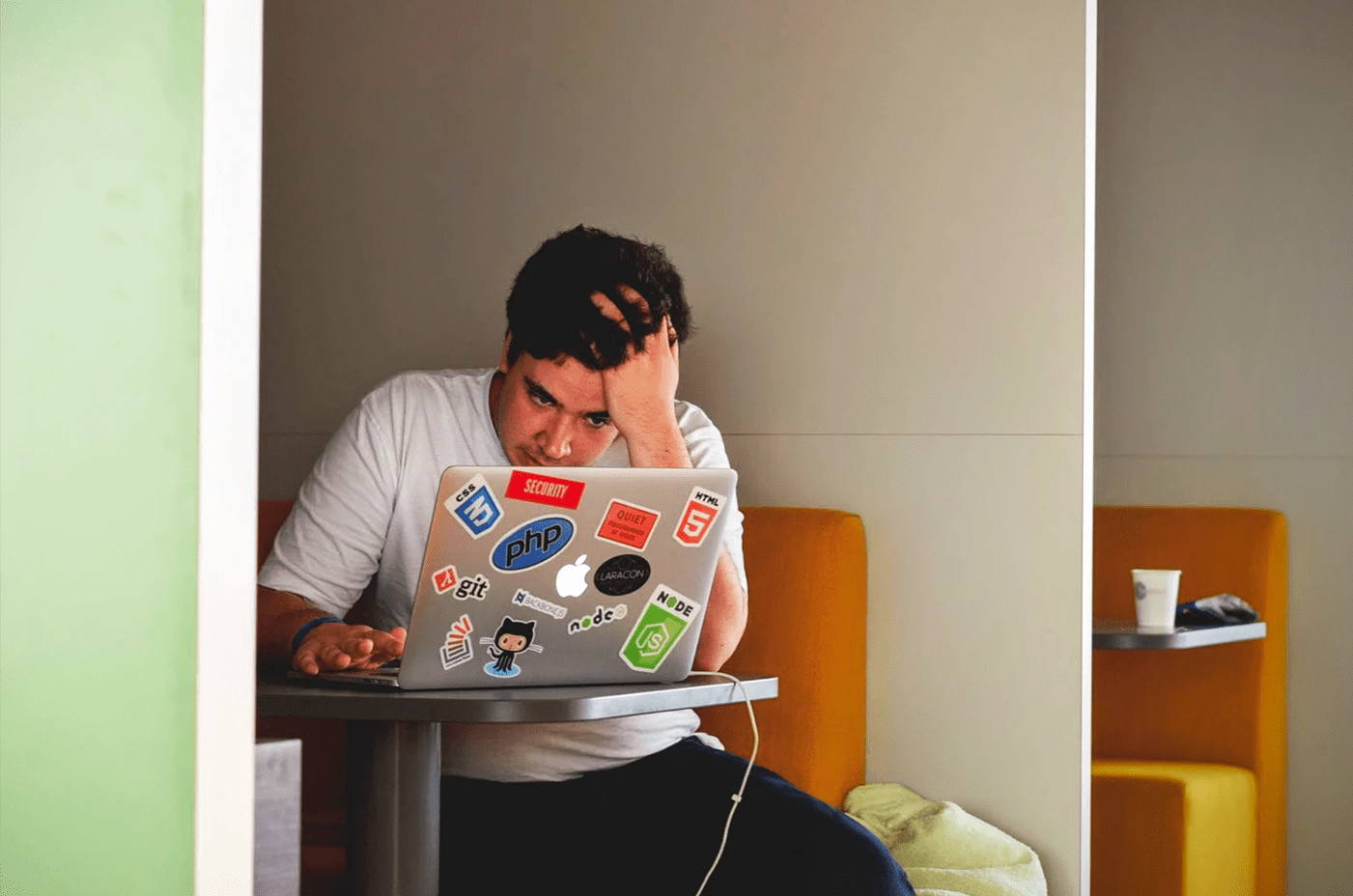man holding his head looking at laptop covered in stickers